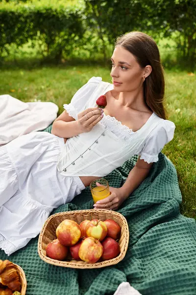 A young beautiful woman relaxes on a picnic blanket while savoring fresh strawberries and juice. — Stock Photo