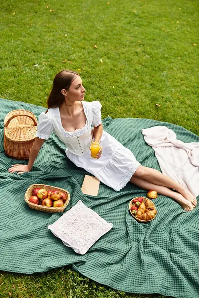 Young woman relaxes on a green blanket, savoring drinks and tasty treats under the sun. — Stock Photo