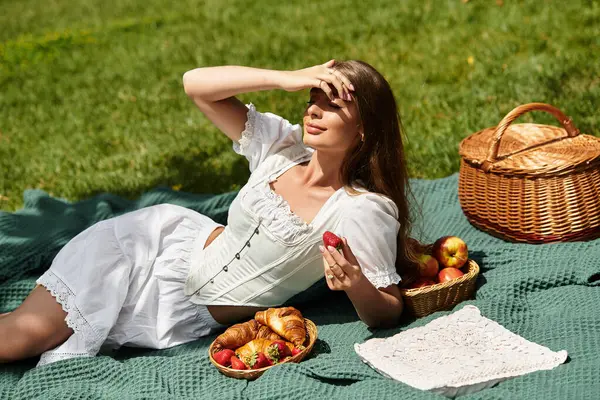 A young beautiful woman relaxes on a blanket, delighting in strawberries and croissants outdoors. — Stock Photo