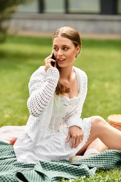 A young woman relaxes on a picnic blanket in a lush park, engaged in a phone conversation. — Stock Photo