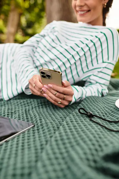 A young woman relaxes at a picnic, enjoying her phone in a vibrant park. — Stock Photo