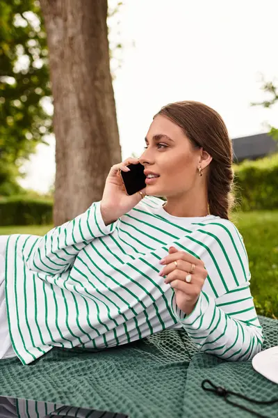 A young woman relaxes on a picnic blanket, enjoying a call in the sunny outdoors. — Stock Photo