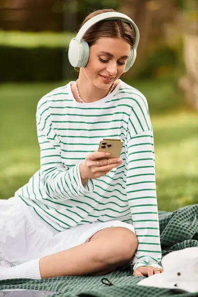 A young beautiful woman relaxes on a picnic blanket, immersed in her music, smiling gently. — Stock Photo