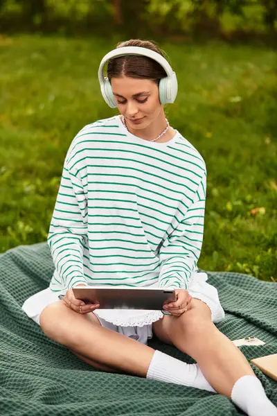 Una joven hermosa mujer se relaja en una manta de picnic, inmersa en su música en el parque. - foto de stock