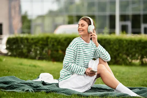 Молодая женщина улыбается, слушая музыку на пикнике в зеленом парке. — Stock Photo