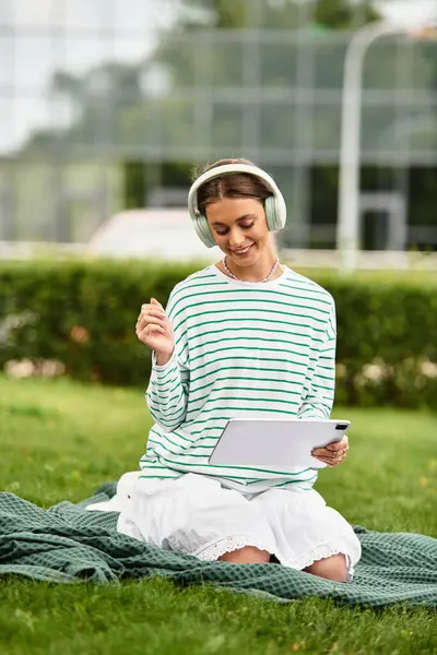 Beneath the warm sun, a young woman relaxes on a blanket, immersed in music while smiling. — Stock Photo