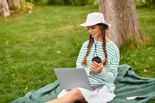 A young and beautiful woman relaxes outdoors, sipping coffee while working on her laptop. — Stock Photo