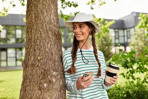 A young beautiful woman relaxes under a tree while sipping her drink and enjoying the outdoors. — Stock Photo