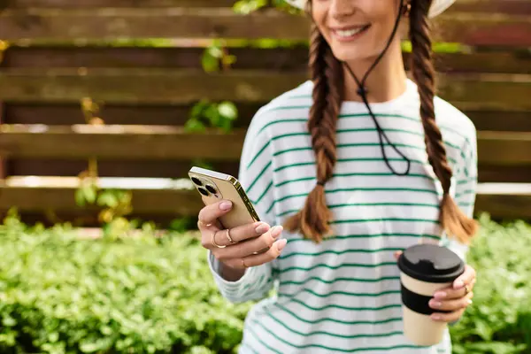 A young beautiful woman smiles while holding her phone and coffee during a picnic with friends. — Stock Photo