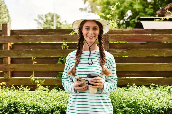 A young woman dressed casually holds a coffee cup while smiling in a vibrant park setting — Stock Photo