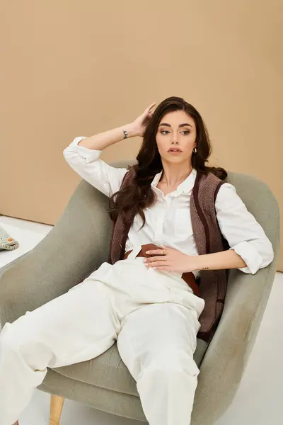 A stylish young woman sits gracefully in a cozy chair, showcasing her chic outfit. — Stock Photo