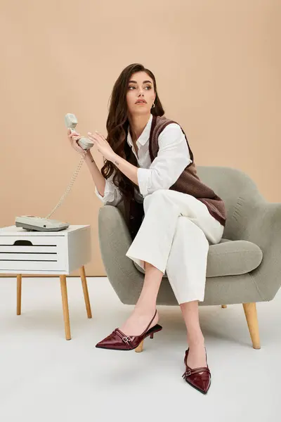 Young woman in fashionable attire sits gracefully, holding a vintage telephone in a minimal studio. — Stock Photo