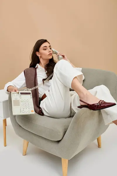 A beautiful young woman sits comfortably in a stylish chair, engaged in a phone conversation. — Stock Photo