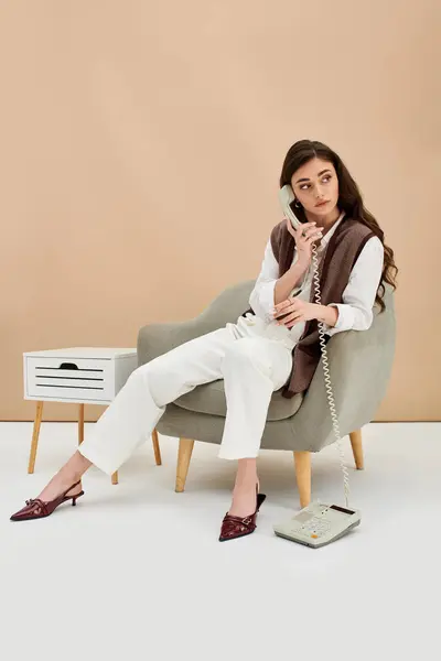 A stylish young woman sits comfortably, talking on the phone in a studio. — Stock Photo