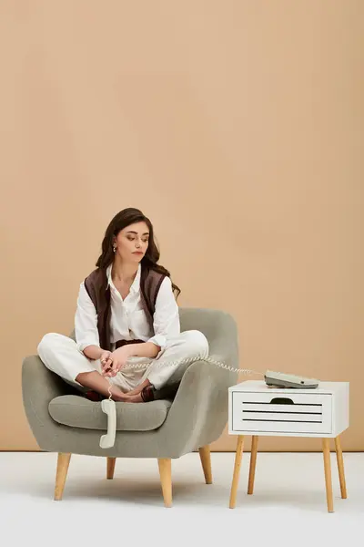 A young woman with long brown hair relaxes in a stylish armchair in a chic studio. — Stock Photo