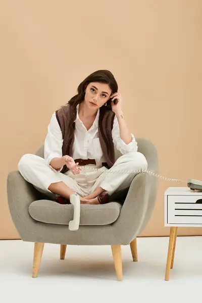 A young woman with long brown hair relaxes in a stylish chair, dressed in a trendy outfit. — Stock Photo