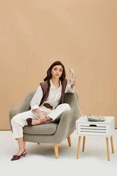 A fashionable young woman with long brown hair relaxes while holding a vintage phone in a studio. — Stock Photo