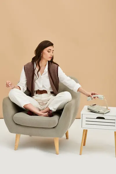 A beautiful woman with long brown hair sits thoughtfully in a cozy studio, dressed fashionably. — Stock Photo