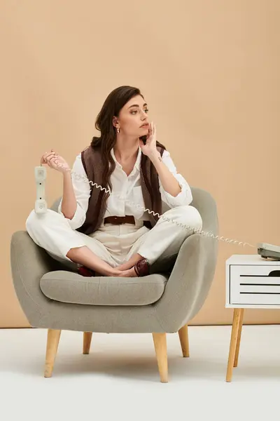 Young woman with long brown hair sits thoughtfully in a chair, engaging on a phone call. — Stock Photo