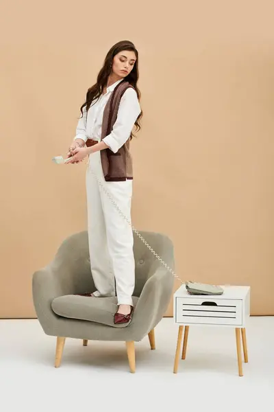 A fashionable young woman stands on a chair with a retro phone, exuding confidence and elegance. — Stock Photo