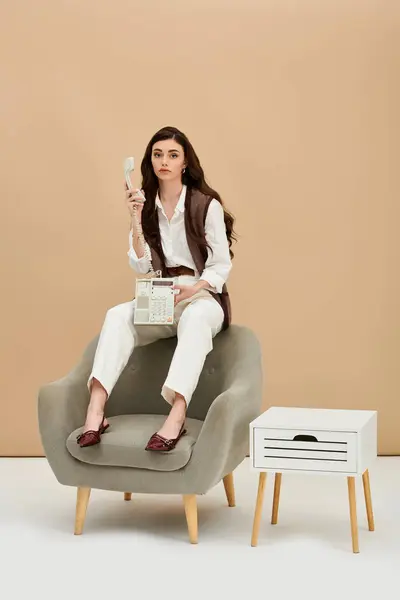 A young woman in modern fashion sits on a cozy chair, holding a vintage phone. — Stock Photo