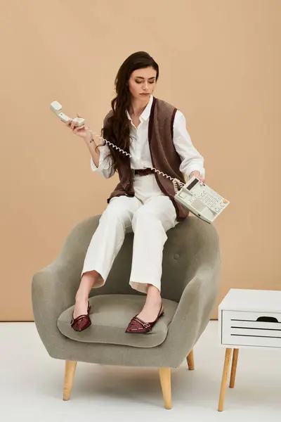 A stylish young woman in fashionable attire sits on a cozy chair, making a phone call. — Stock Photo
