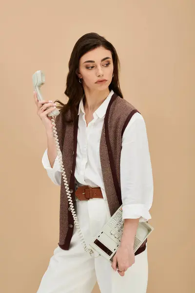 Beautiful young woman stands confidently holding a vintage phone, dressed in fashionable attire. — Stock Photo