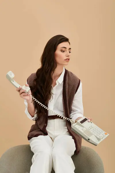 Beautiful young woman with long hair and fashionable outfit sits while talking on the phone. — Stock Photo