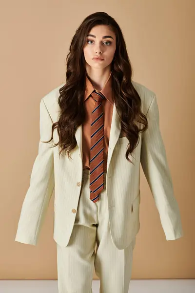 A beautiful young woman with long brown hair showcases her fashionable suit with a tie in a studio. — Stock Photo