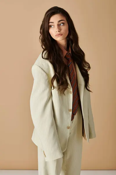 A stylish young woman flaunts her long brown hair in a chic suit, radiating confidence. — Stock Photo