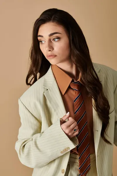 A young woman with long brown hair models a fashionable suit and tie against a warm backdrop. — Stock Photo