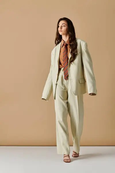 A confident young woman with long brown hair models a stylish oversized suit with a tie. — Stock Photo