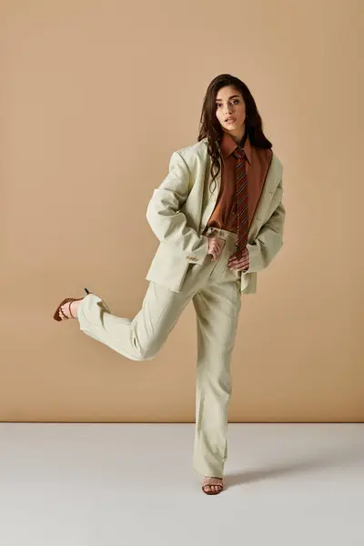 Young woman with long brown hair poses confidently in a fashionable suit and tie within a studio. — Stock Photo