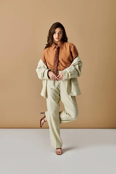 A fashionable young woman with long brown hair models an elegant suit with a tie in a studio. — Stock Photo