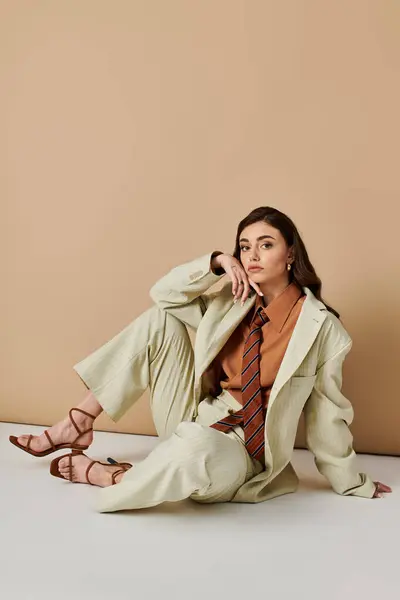 A young woman with long brown hair sits elegantly in a trendy outfit in a studio setting. — Stock Photo