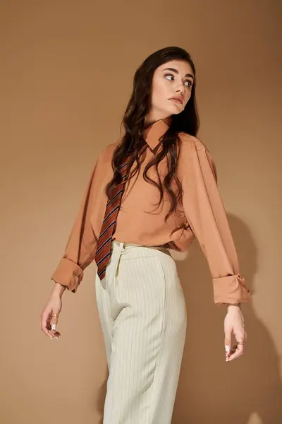 A young woman with long brown hair models a fashionable outfit with a tie in a studio setting. — Stock Photo