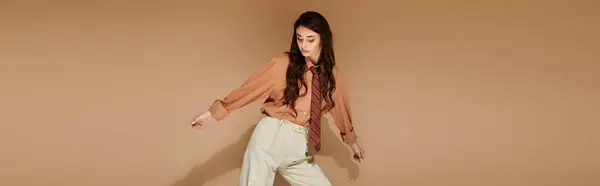 A beautiful young woman with long brown hair poses in a fashionable attire with a tie in a studio, banner — Stock Photo