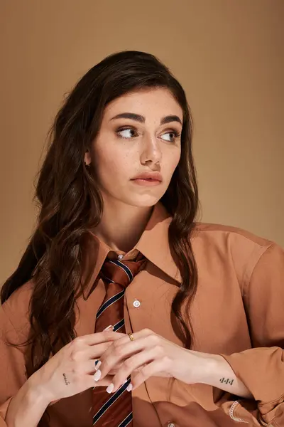 A young woman with long brown hair showcases a fashionable attire with a tie in a stylish studio. — Stock Photo