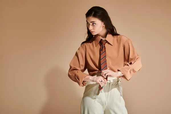 A beautiful young woman with long brown hair showcases a fashionable attire with a tie in the studio. — Stock Photo