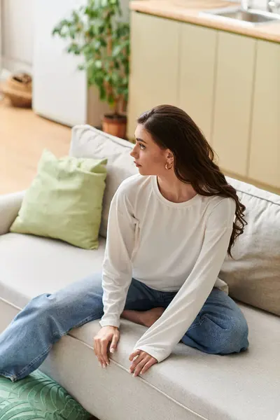 A beautiful woman sits comfortably on the couch, enjoying a peaceful moment at home. — Stock Photo