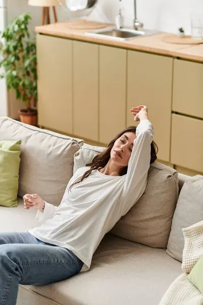 A brown-haired young woman relaxes on her couch in her peaceful home. — Stock Photo