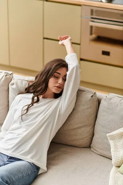 A beautiful young woman with brown hair enjoys a restful moment on her couch at home. — Stock Photo