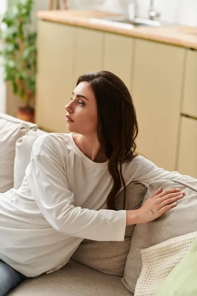 A young woman with brown hair relaxes on a sofa in her cozy apartment, savoring her time at home. — Stock Photo