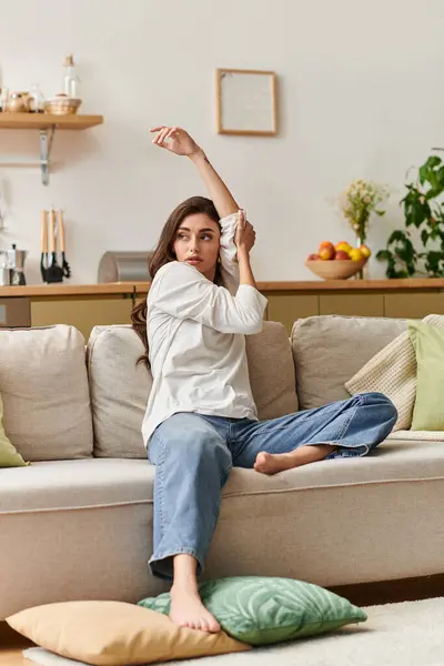 A beautiful young woman with brown hair relaxes at home, stretching on her comfortable couch. — Stock Photo