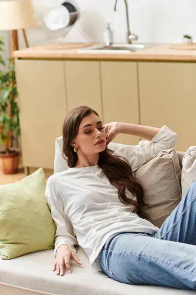 A young woman with brown hair relaxes on her couch, embracing a peaceful moment at home. — Stock Photo