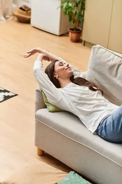 A young woman with brown hair comfortably rests on a sofa, enjoying a peaceful moment at home. — Stock Photo