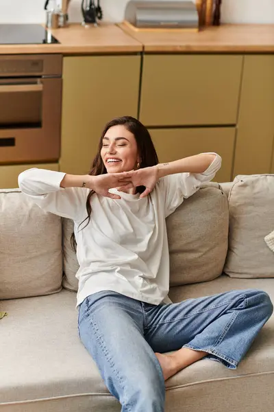 A beautiful young woman with brown hair rests comfortably on her couch, smiling and relaxed. — Stock Photo