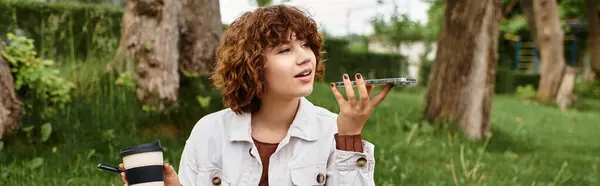 Curly-haired woman relaxes on a blanket in a green park, sipping her drink and using her phone, banner — Stock Photo