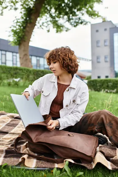 Young woman with curly hair works remotely on her laptop in a sunny park setting. — Stock Photo
