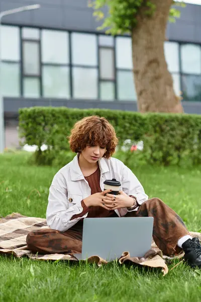 A young woman with curly hair is focused on her laptop while enjoying a warm summer day in the park. — Stock Photo
